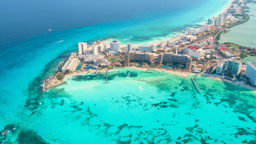 Luftaufnahme von Cancún, Mexiko, mit türkisblauem Wasser, weißen Sandstränden und modernen Hotelanlagen entlang der Küste.