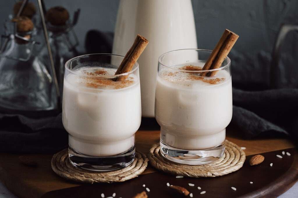 Zwei Gläser mit mexikanischer Horchata, serviert mit Eis und Zimtstangen – klassische Präsentation des Reisgetränks