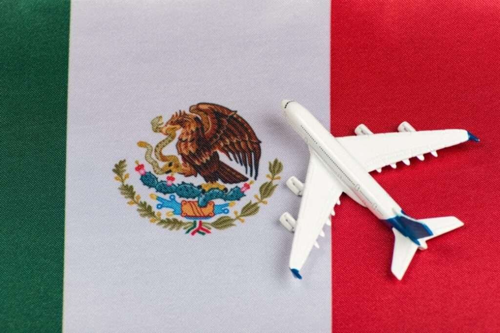 Symbolbild für teure Dinge in Mexiko: Ein Flugzeug liegt auf der mexikanischen Flagge – Hinweis auf Reisekosten
