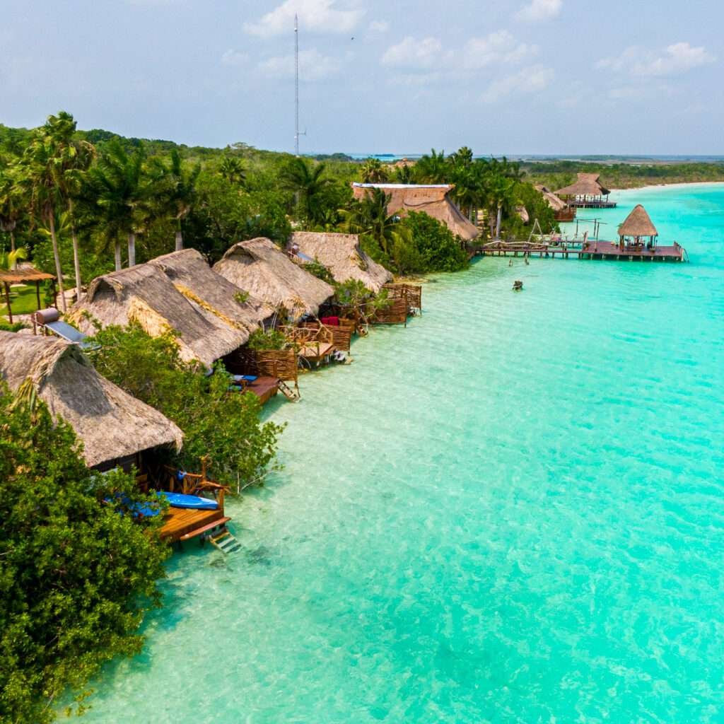 Türkisfarbenes Wasser und strohgedeckte Hütten am Ufer in Bacalar, einem der bekanntesten Pueblos Mágicos Mexikos