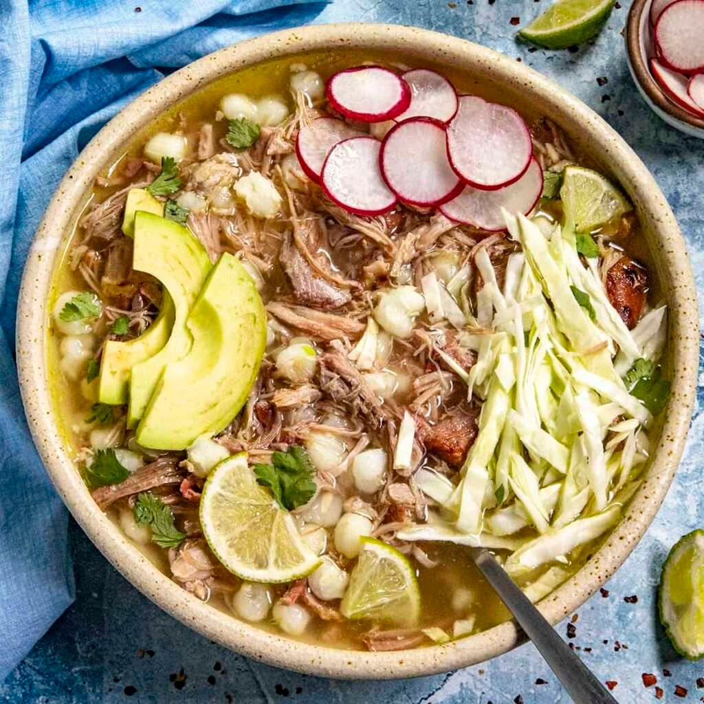 Mexikanische Pozole Blanco mit Fleisch, Avocado, Limetten, Kohl und Radieschen in einer Tonschale