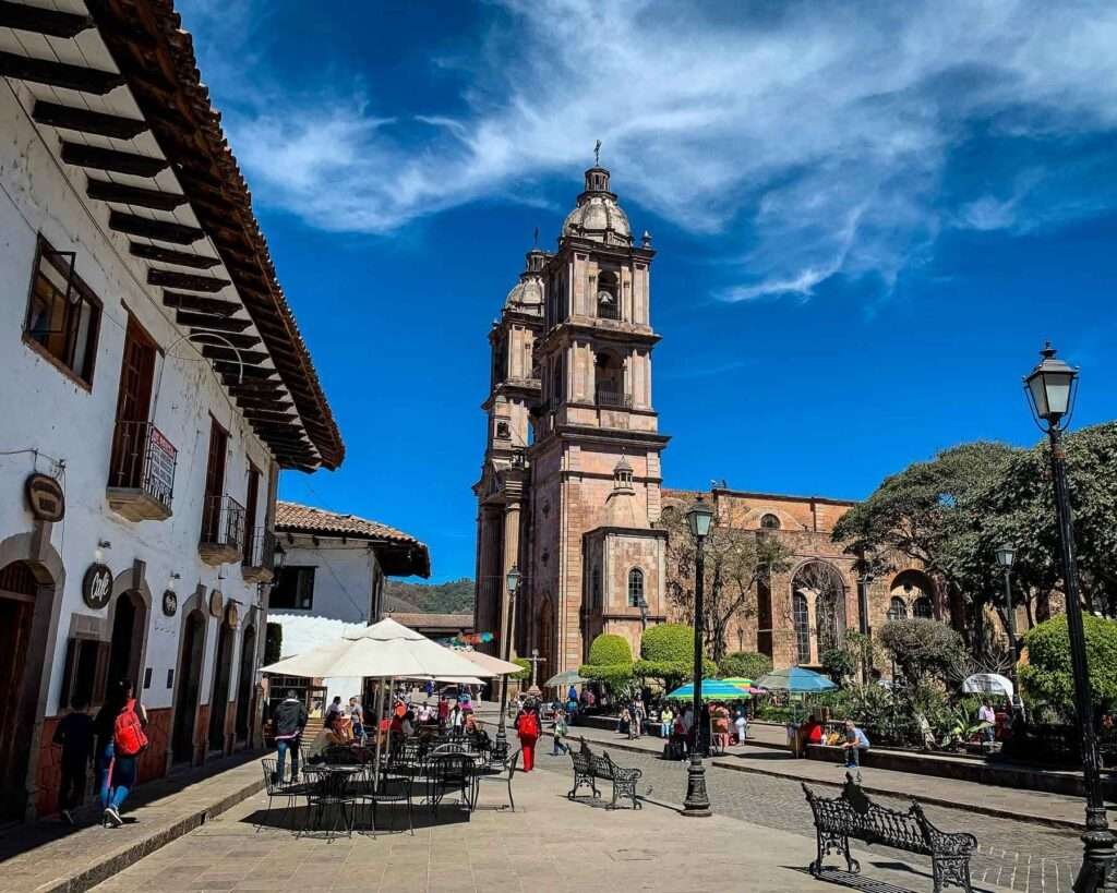 Zentrum von Valle de Bravo mit barocker Kirche und Menschen auf dem Hauptplatz, ein Beispiel für städtische Eleganz in den Pueblos Mágicos