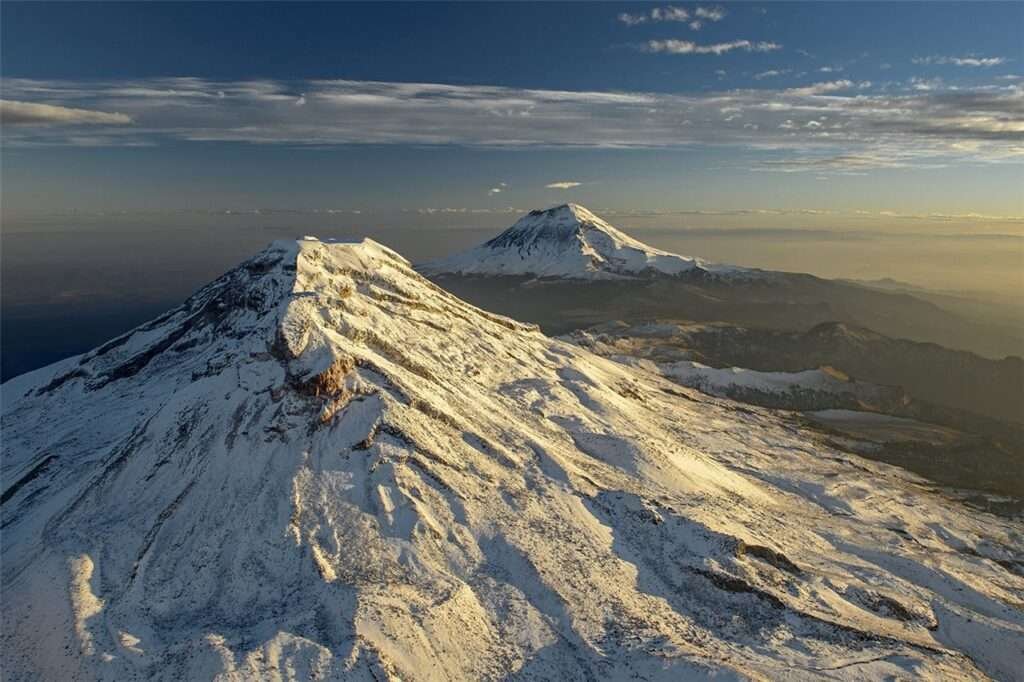 Blick auf die schneebedeckten Vulkane Iztaccíhuatl und Popocatépetl, zwei der drei höchsten Berge Mexikos, unter klarem Himmel bei Sonnenaufgang