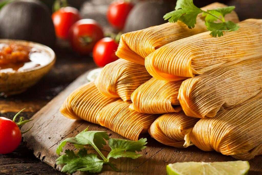Mehrere mexikanische Tamales eingewickelt in Maisblätter auf einem rustikalen Holztisch