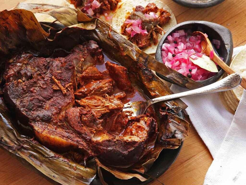 Cochinita Pibil serviert im Bananenblatt mit eingelegten roten Zwiebeln und Tortillas